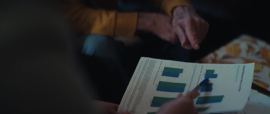 A close-up of two individuals analyzing and discussing a financial report with bar graphs in slow motion
