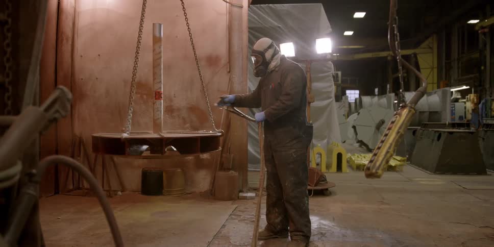 A man with a mask spins a metal cylinder around as he spray paints it