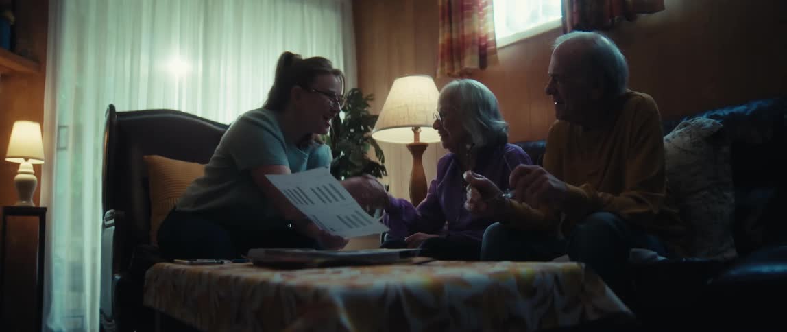 A friendly female advisor explains paperwork to a senior couple in their home, ending the successful meeting with a handshake