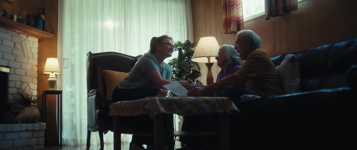 A caring professional consults with a happy senior couple in their living room, leading to a joyful agreement and a handshake