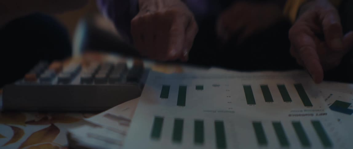 A detailed, slow-motion shot shows two people pointing at and analyzing a printed bar graph during a meeting