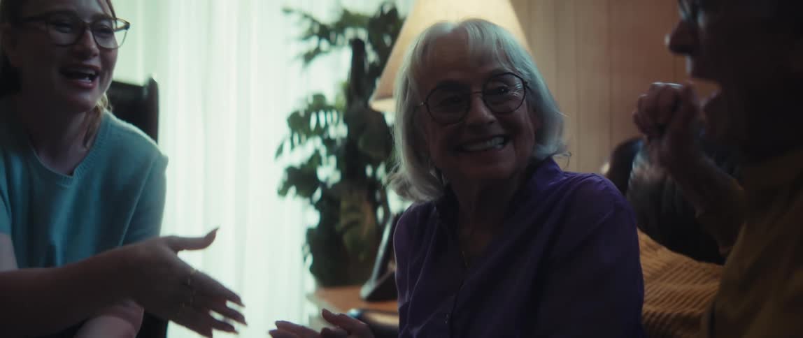 A young woman explains a document to an elderly couple, leading to a joyful handshake and an emotional hug in their living room