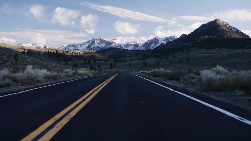 A scenic point-of-view drive on an open highway through a valley towards a majestic snow-capped mountain range
