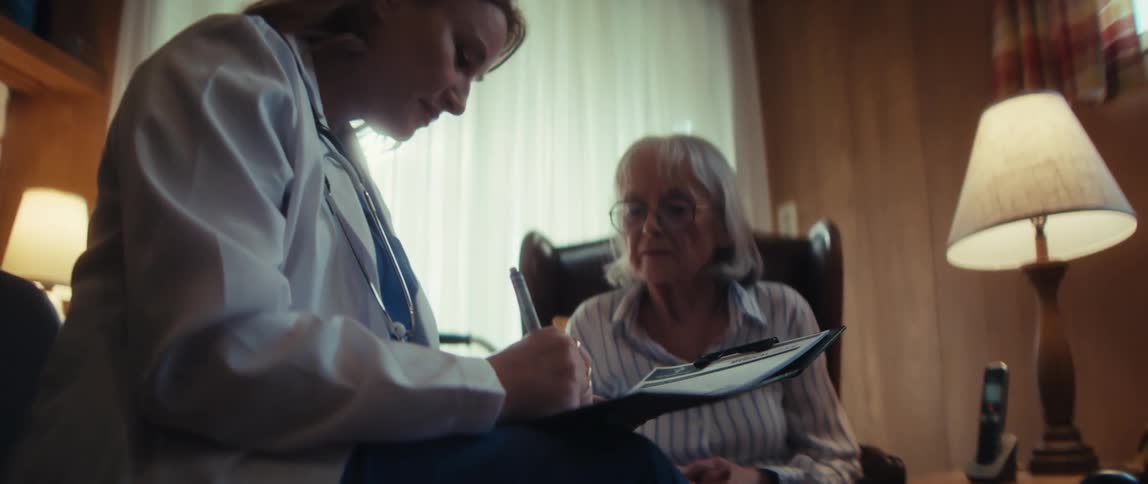 Cinematic shot of a female doctor attentively listening and writing on a clipboard during a house call with a senior woman