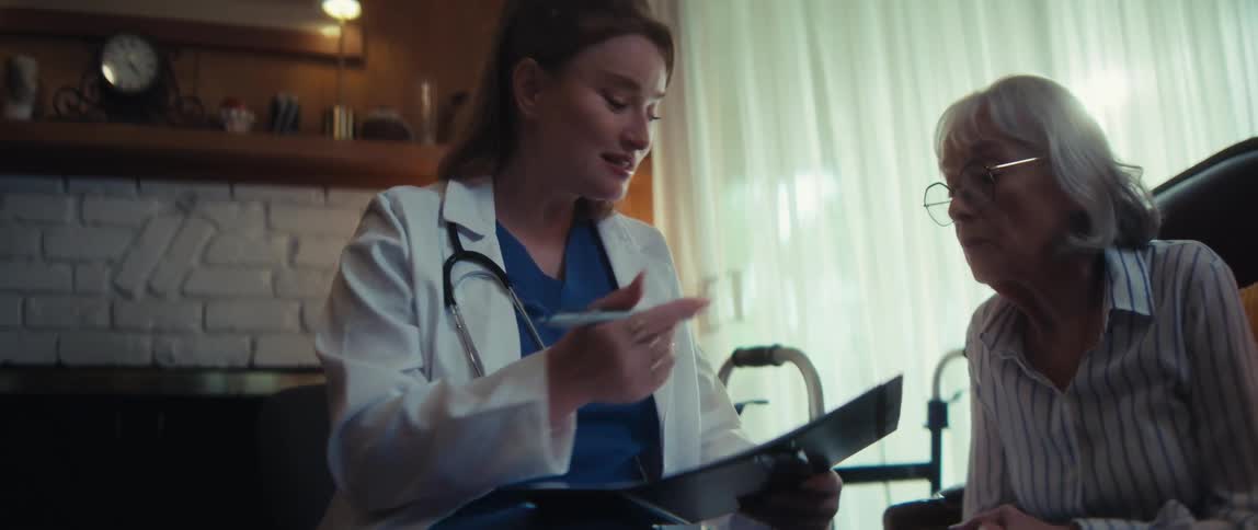 A caring female doctor discusses medical results on a clipboard with her elderly patient during a home health care visit