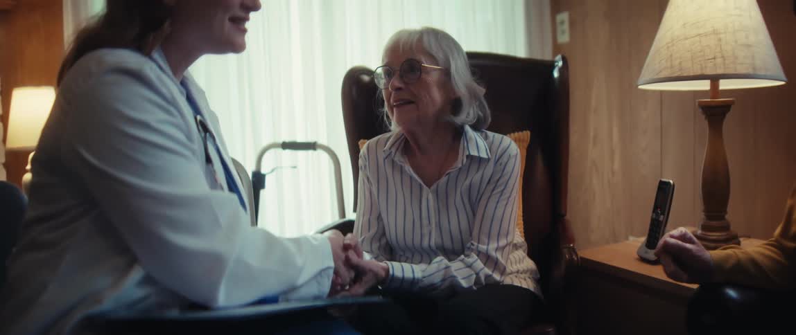 A compassionate female doctor holds an elderly patient's hand during a home visit, offering comfort and support