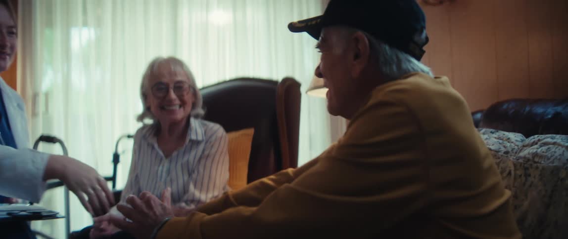 A friendly doctor on a house call warmly shakes hands with an elderly Vietnam veteran as his happy wife looks on