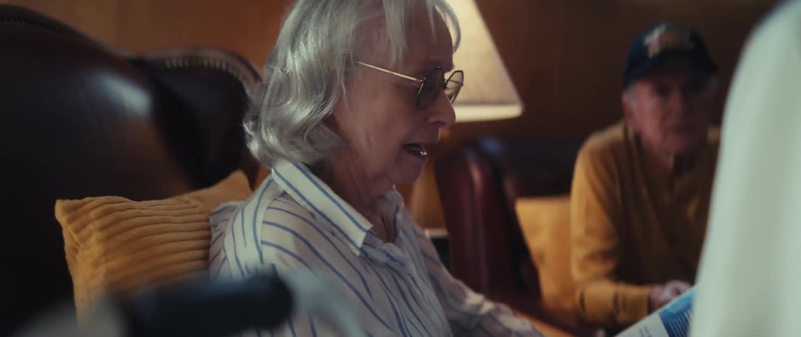 A senior woman reads a letter to her husband, a Vietnam veteran, in their warmly lit living room