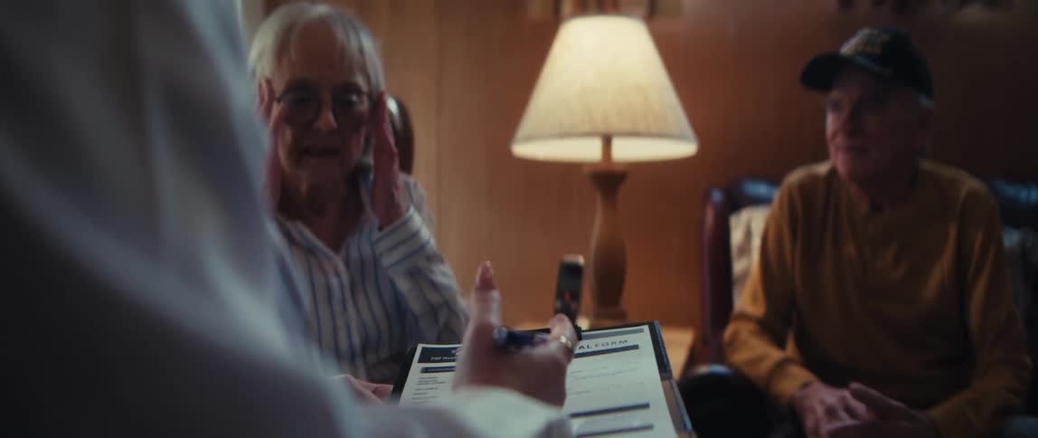 Over the shoulder of a doctor filling out a medical form while an elderly couple reacts to difficult news in a consultation