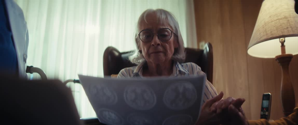 A somber elderly woman looks at her brain scan results while being comforted by her loved one and a doctor