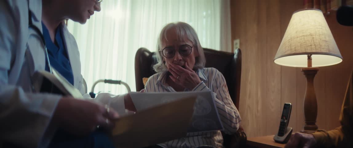 A doctor delivers a serious diagnosis to a concerned elderly couple by reviewing brain scans during a home visit
