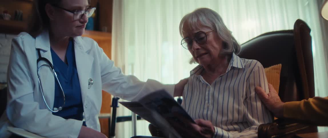A compassionate doctor and a loving husband comfort an elderly woman as she receives difficult medical results at home