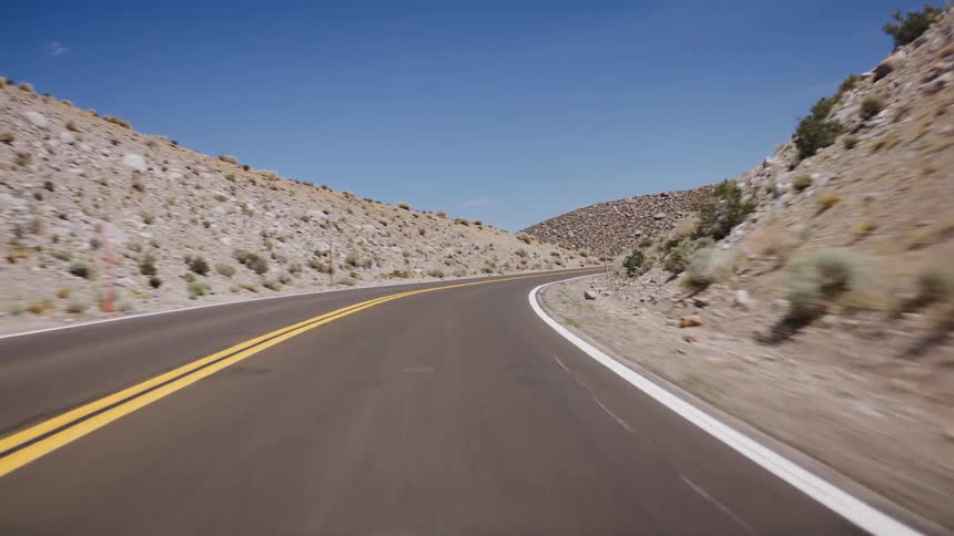 A smooth point-of-view drive along a winding highway through a rocky, arid mountain pass on a sunny day