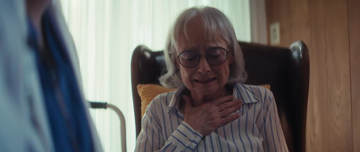A distraught elderly woman reacts with sadness after receiving difficult medical news from a doctor during a house call