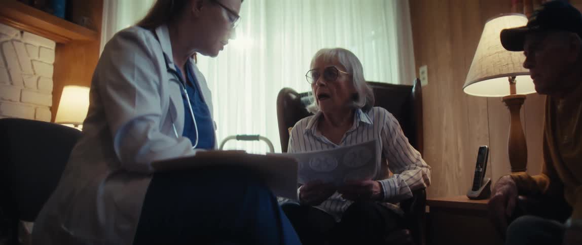 A female doctor reviews difficult brain scan results with a senior couple in their home, delivering somber news