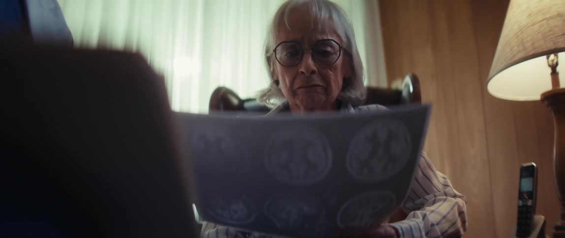 An elderly woman looks at her brain scans with a concerned expression as a doctor delivers a serious medical diagnosis