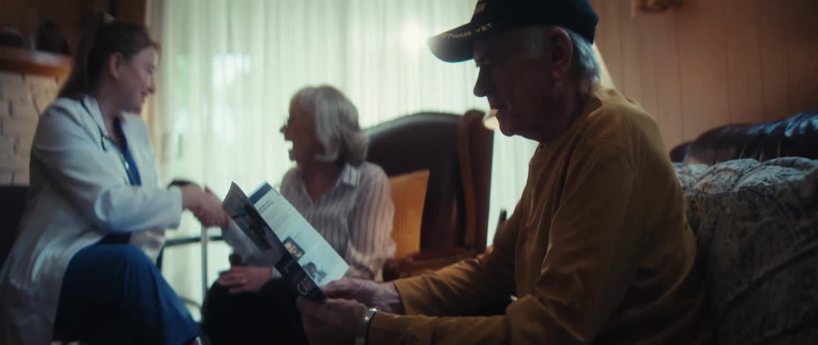 A home healthcare nurse explains a medical brochure to an elderly Vietnam veteran and his wife in their cozy living room