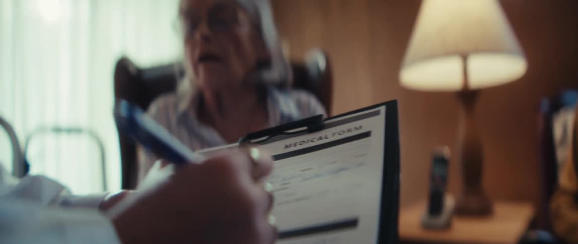 A doctor fills out a medical form for an elderly veteran and his wife during a home visit consultation