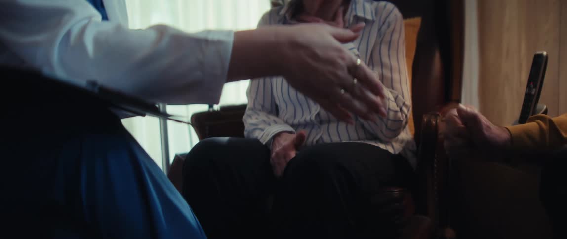 A compassionate doctor provides reassurance to a grateful elderly couple, shaking their hands during a supportive home visit