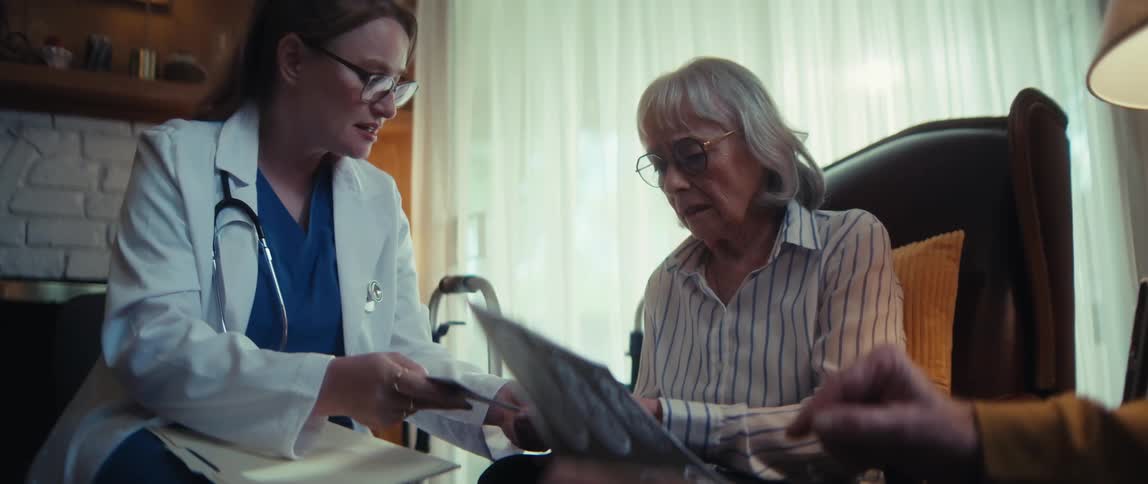 A compassionate doctor explains a serious diagnosis to an elderly couple at home while reviewing their brain scans