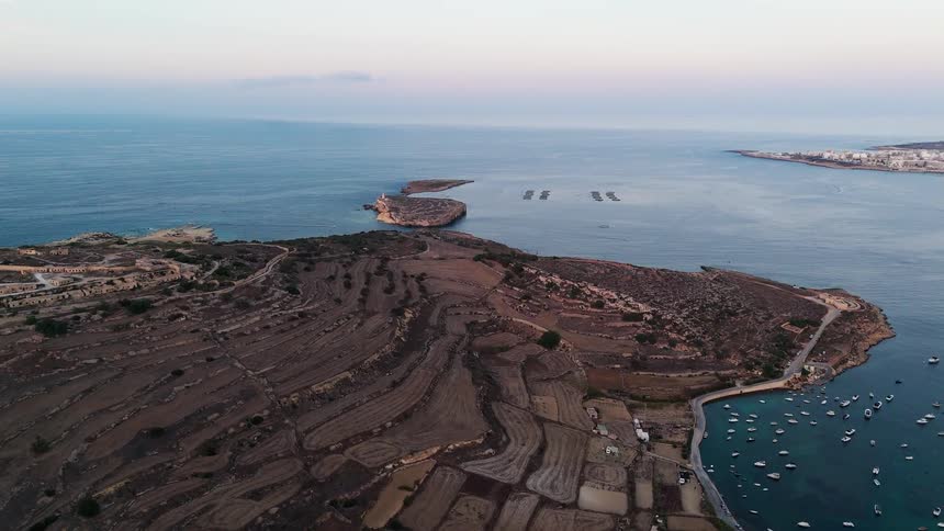 A stunning aerial view captures the terraced farmlands and a boat-filled bay along a rugged Mediterranean coastline at sunset