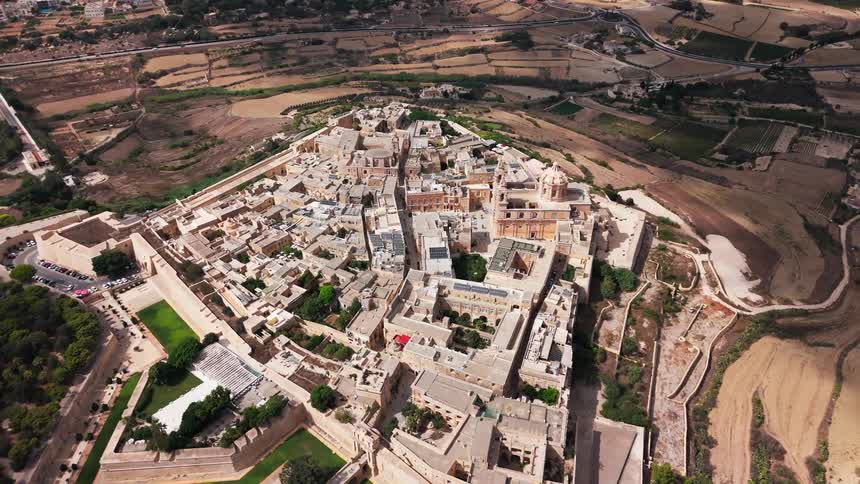 A slow aerial pullback reveals the magnificent ancient walled city of Mdina, Malta, surrounded by the island's rural landscape