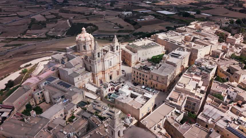 An aerial drone shot slowly pushes in over the historic walled city of Mdina in Malta, focusing on the beautiful St. Paul's Cathedral