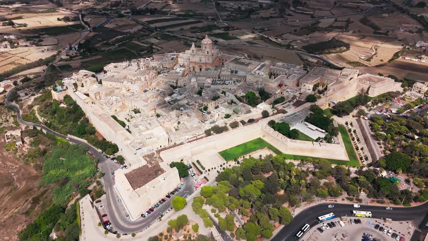 An expansive aerial shot captures the historic fortified city of Mdina, Malta, nestled on a hilltop amidst the island's rural scenery