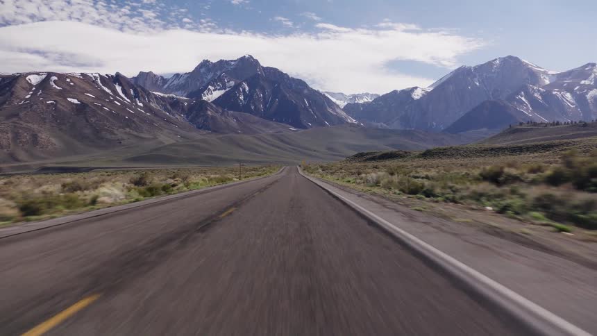 A fast-paced point-of-view drive along an endless road toward snow-covered mountains in a vast, open landscape