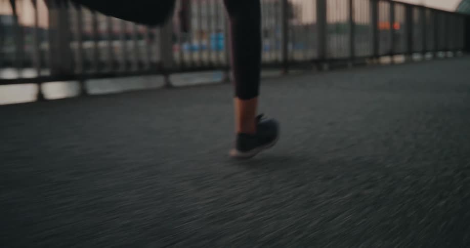 Low angle close-up of a runner's legs and feet in motion on a paved city bridge