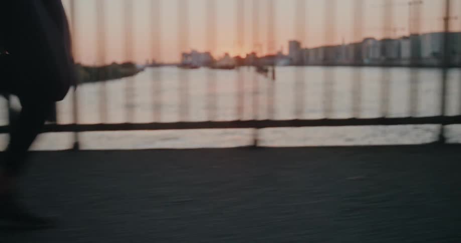 Close-up slow motion shot of a runner's legs in motion on a city bridge during a beautiful sunset