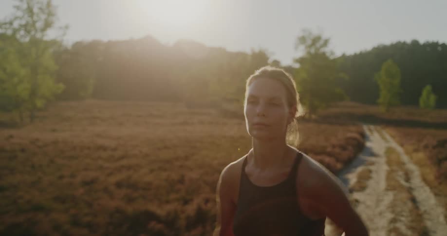 Close-up slow-motion shot of a determined woman running on a dirt path through a field of heather during a beautiful sunrise