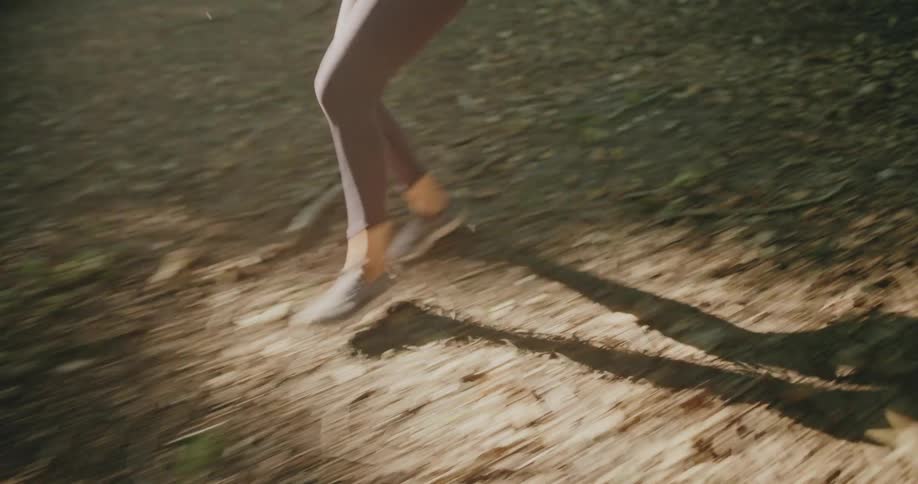 Side view of an athletic woman running in slow motion through a sun-dappled forest