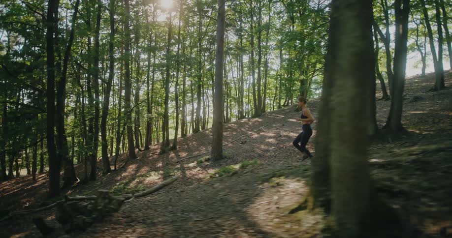 Slow motion side view of a fit woman trail running uphill through a beautiful sunlit forest