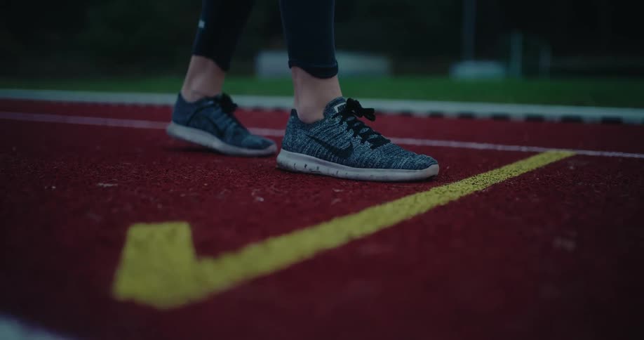 Low angle slow motion shot of a runner's shoes taking off from the starting line on a red track