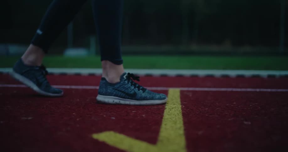 A close-up, slow-motion shot of a runner's feet in sneakers as they take off from the starting line on a red track