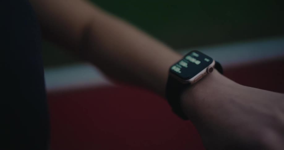 An athlete checks their running metrics and progress on a smartwatch while sitting at a stadium track