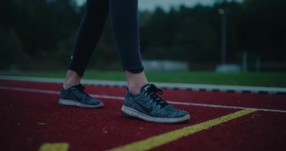 A close-up of a runner's feet in sneakers walking and then starting to sprint on a red track in slow motion