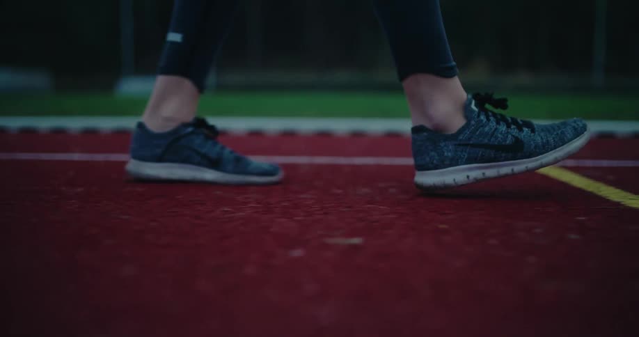 Slow motion close-up of a runner's shoes as they warm up and walk on a red running track