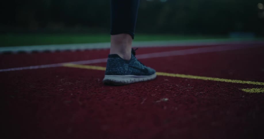 A runner's feet in sneakers start a sprint on a red athletic track in a dramatic low-angle close-up