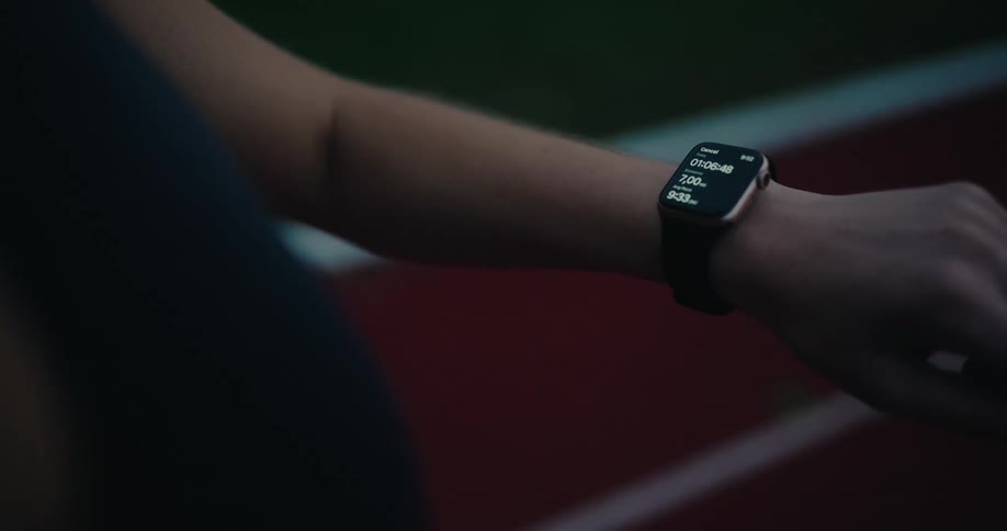 A runner checks their smartwatch while training on a track during the evening