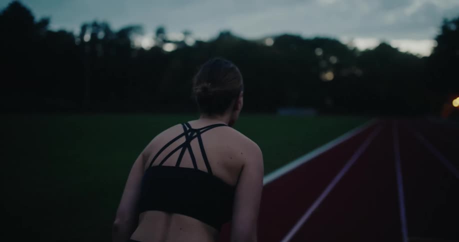 A female athlete gets into position and starts sprinting down a running track in slow motion as the shot goes out of focus
