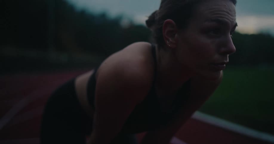 A determined female athlete pauses to catch her breath on a running track during an evening workout