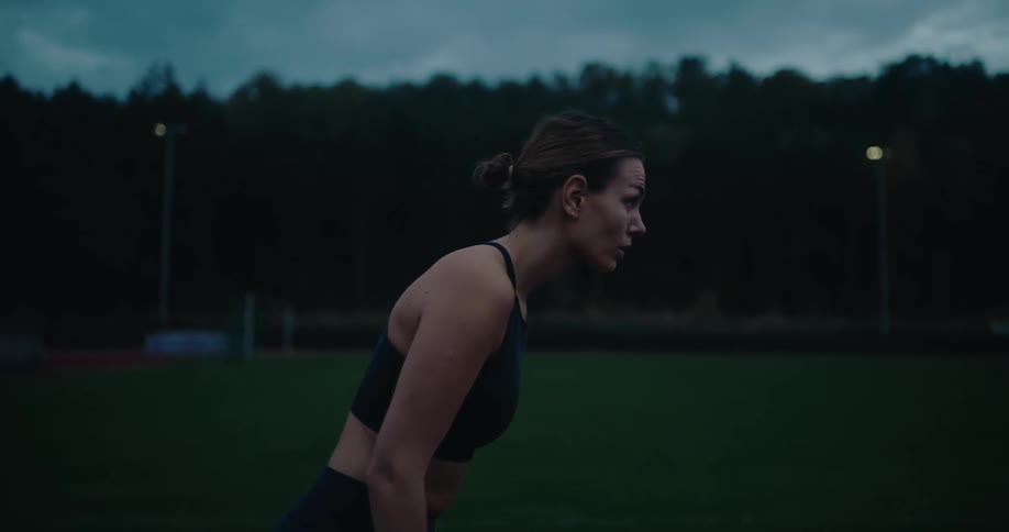 A female athlete in a low starting position explodes into a sprint on a track in the early morning in slow motion