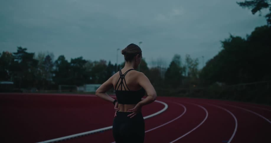 An athletic woman takes a contemplative pause on a red running track during an early morning or evening workout session