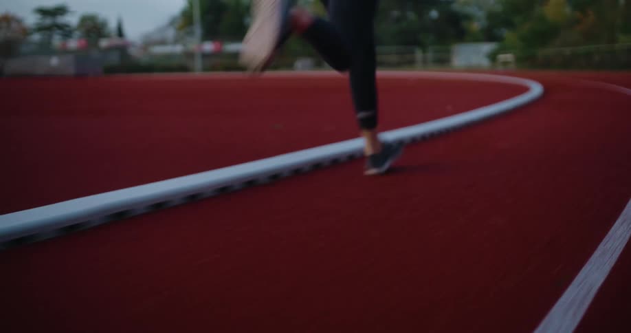 Low-angle slow-motion footage of a female runner's legs as she sprints around a red athletic track
