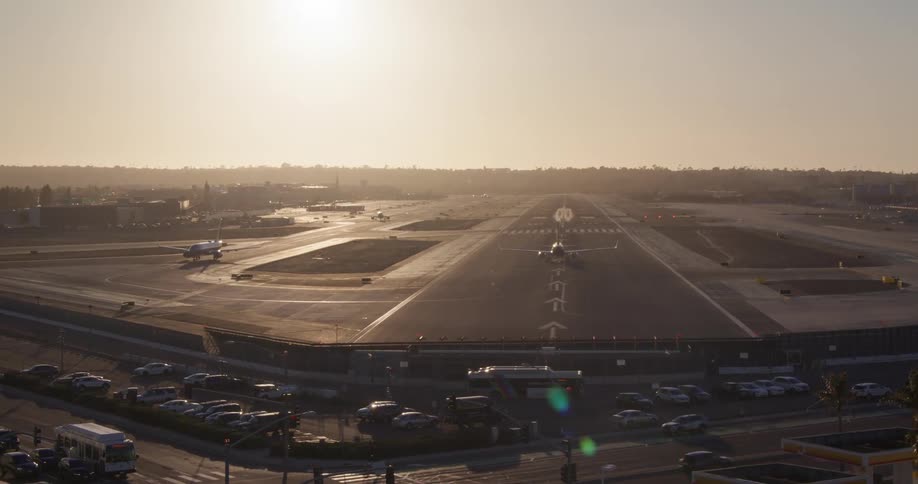 A passenger jet taxis down the runway for takeoff at a major airport with city traffic in the foreground during a hazy sunset