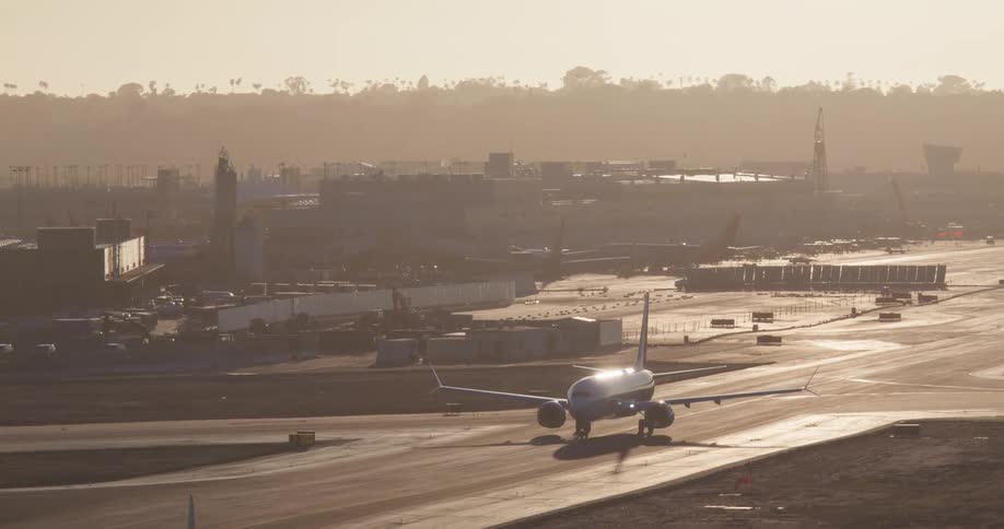 A passenger airplane taxis on the airport runway, bathed in the warm, hazy light of sunset