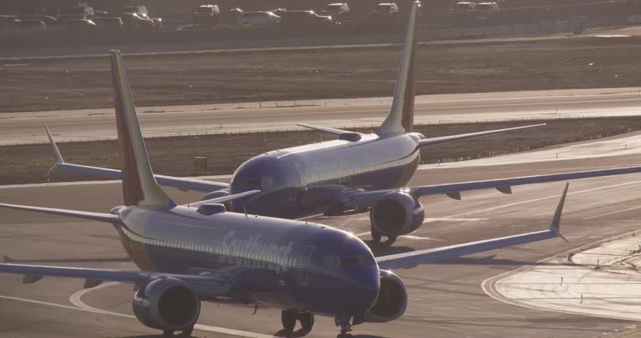 Two Southwest Airlines planes sit stationary on the tarmac at an airport during golden hour