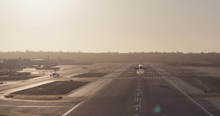 A commercial jetliner makes a smooth landing on an airport runway against a hazy, sunlit sky